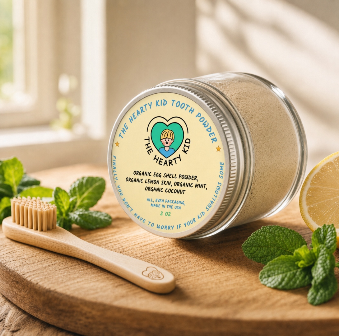 The Hearty Kid Lemon + Mint Tooth Powder jar on a wooden surface with mint leaves and a fresh lemon